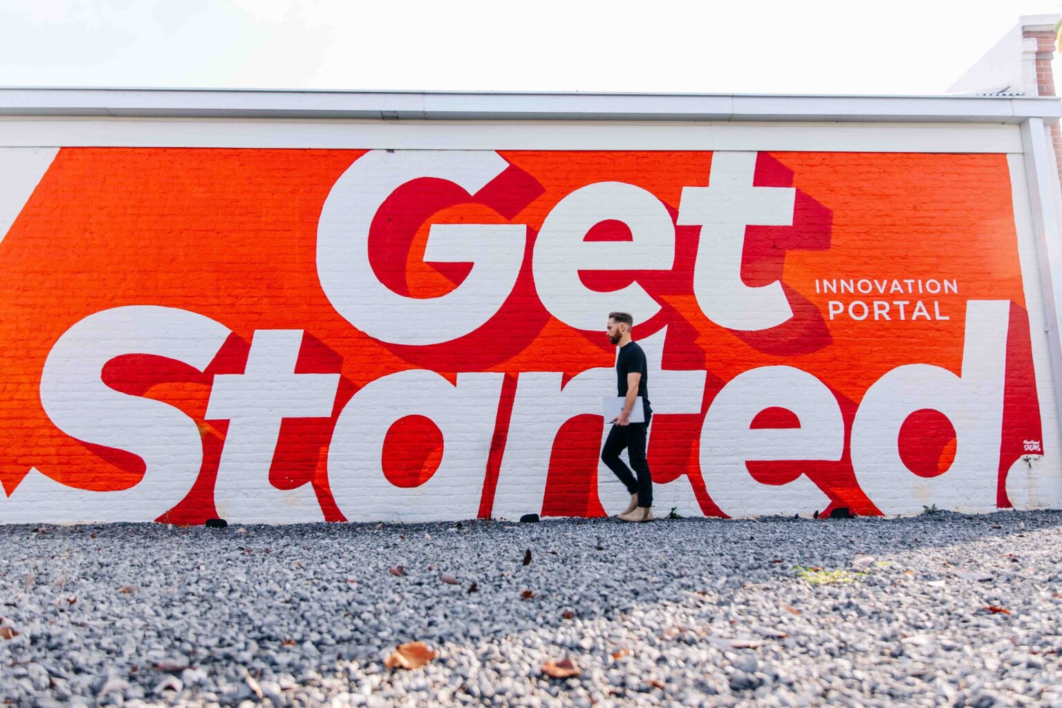An image of a man walking in front of a wall with a mural that reads Get Started.